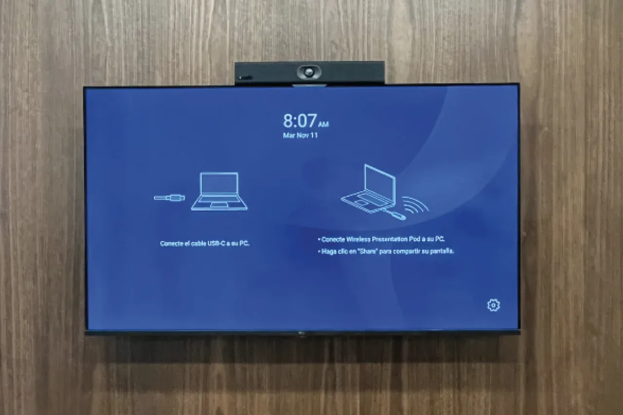 Pantalla de la sala de reuniones con la barra Yealink encima, mostrando en el escritorio las instrucciones para compartir contenido sin cables.