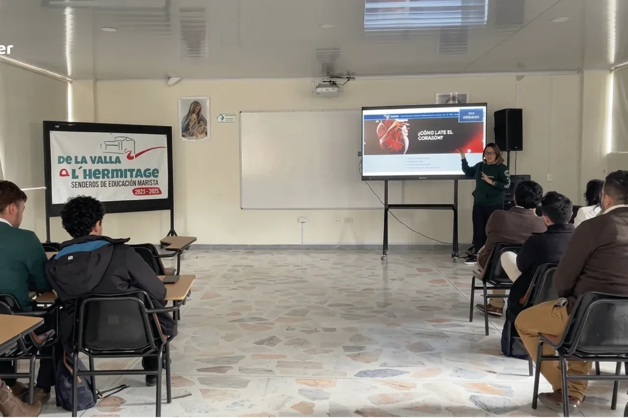 Salón de bachillerato del Colegio Champagnat con estudiantes en sus pupitres siguiendo la clase en la pantalla interactiva encendida junto al tablero.