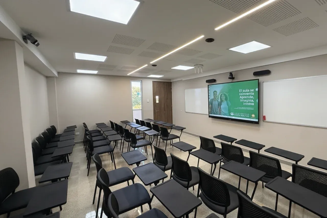Aula amplia de la Universidad Simón Bolívar con pupitres en filas y la pantalla interactiva al frente, con los equipos de audio y cámara en el techo.
