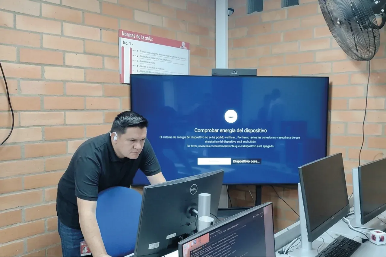 Un docente prepara la sesión desde el puesto de control del aula, con la pantalla y los monitores encendidos.