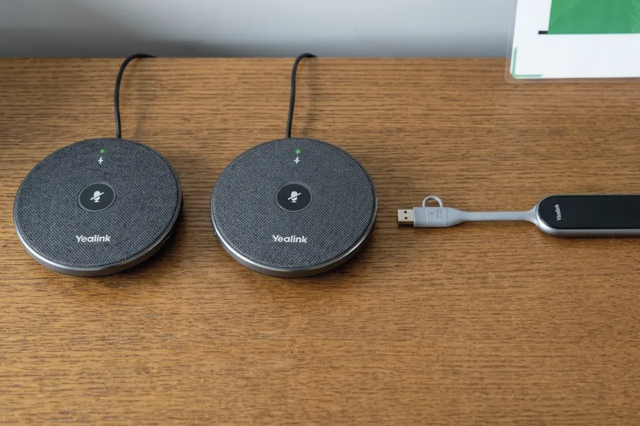 Detalle sobre la mesa: dos micrófonos inalámbricos Yealink VCM36 y el transmisor WPP30 con su cable USB.