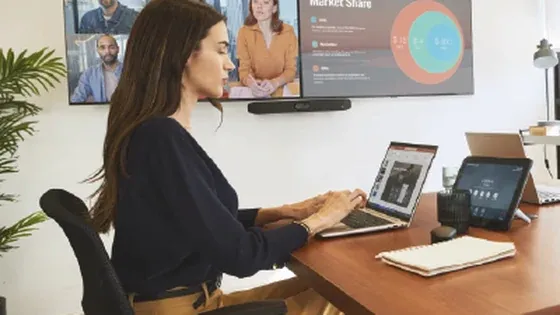 Una persona en videollamada desde su escritorio, con los participantes en la pantalla y una barra Poly debajo
