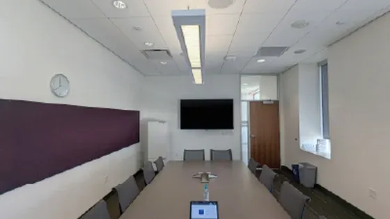 Sala de juntas alargada con micrófono de techo Shure sobre la mesa y una pantalla al fondo