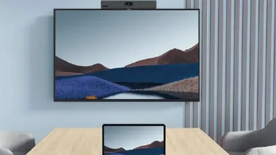 Sala de reuniones con una pantalla y una barra de videoconferencia Yealink montadas en la pared, y un portátil sobre la mesa
