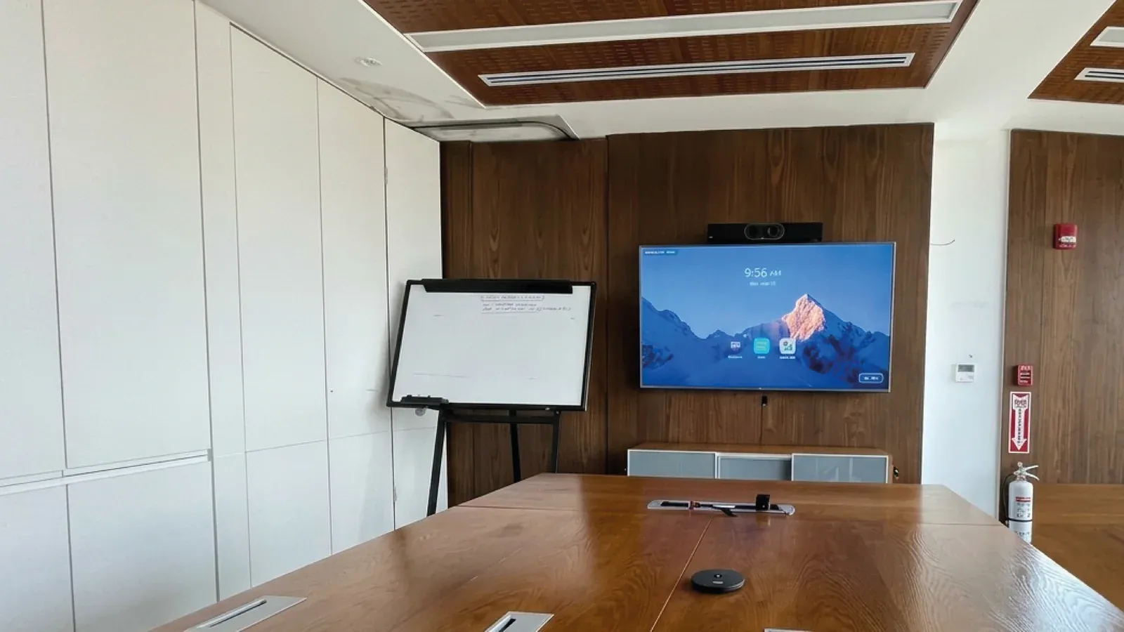 Sala de juntas de SEC Newgate con mesa de madera y la pantalla con barra de videoconferencia Yealink montada sobre el panel de madera del fondo.