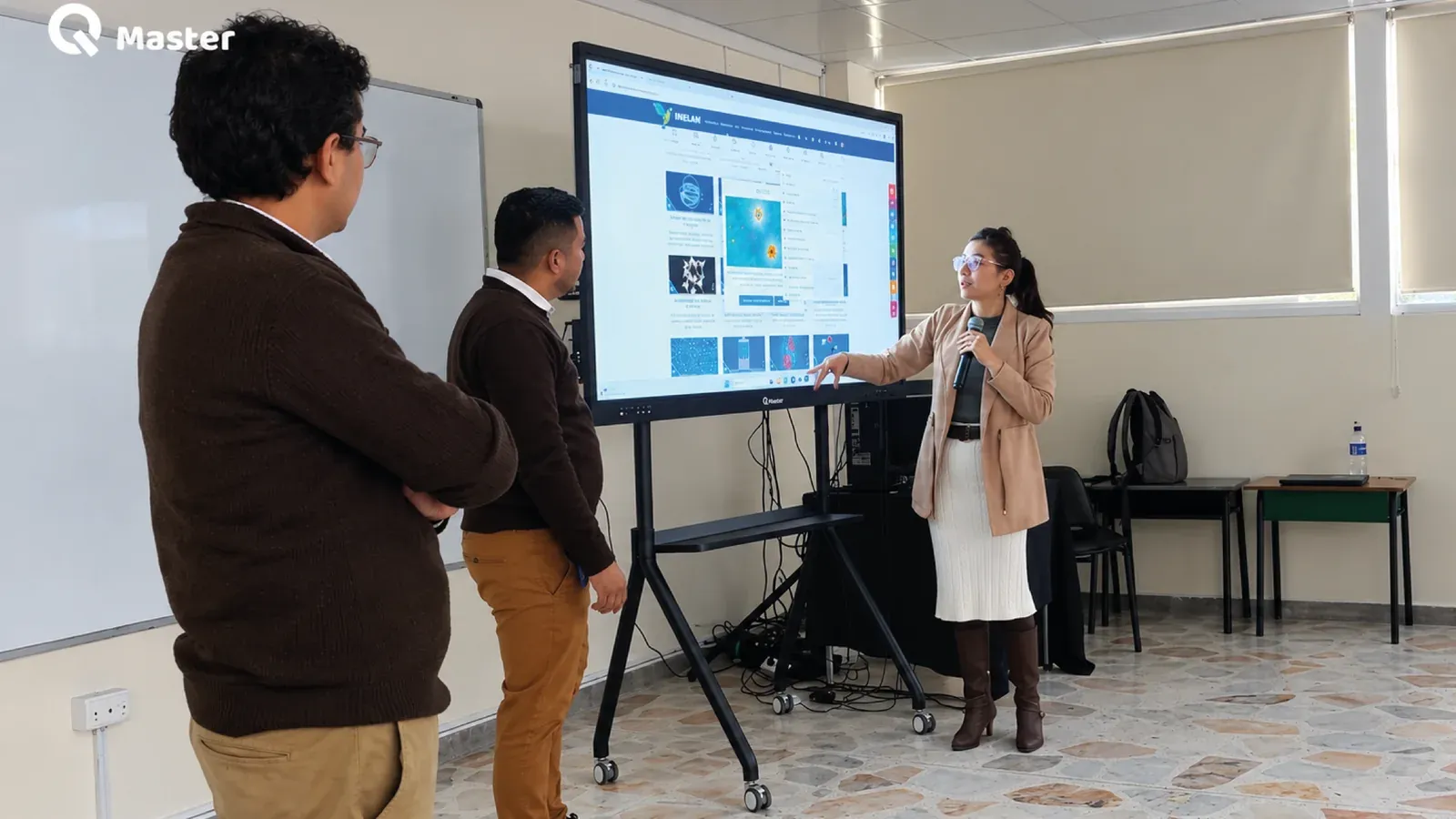 Salón de bachillerato del Colegio Champagnat: una pantalla interactiva QMaster de 86 pulgadas sobre soporte móvil, encendida con material de clase, mientras una docente la opera y dos colegas observan.