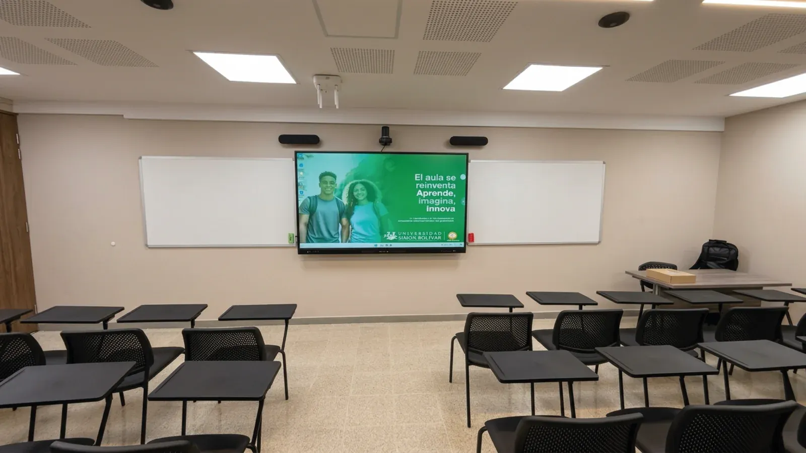Salón de la Universidad Simón Bolívar con pupitres en filas y, al frente, la pantalla interactiva encendida junto al tablero.