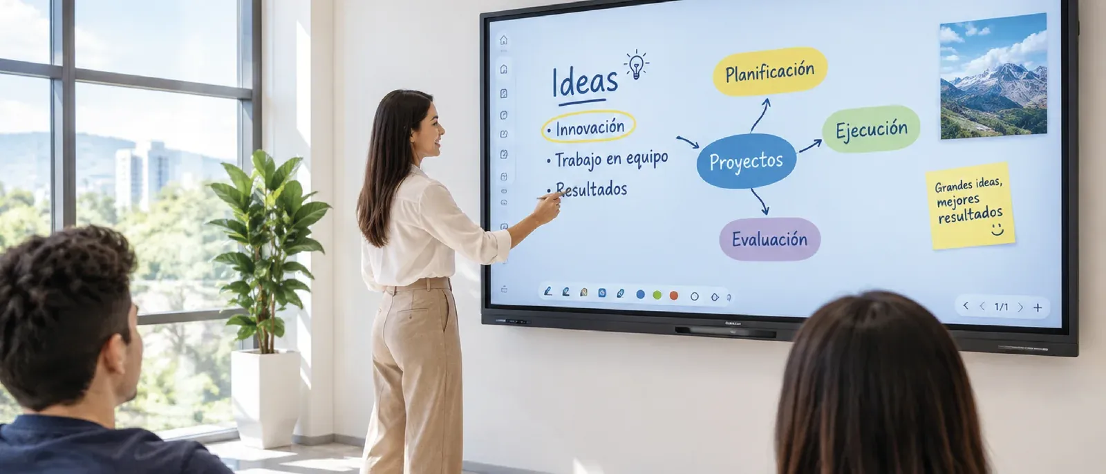 Una presentadora señala un mapa de ideas en una pantalla interactiva QMaster montada en pared, frente a dos asistentes sentados